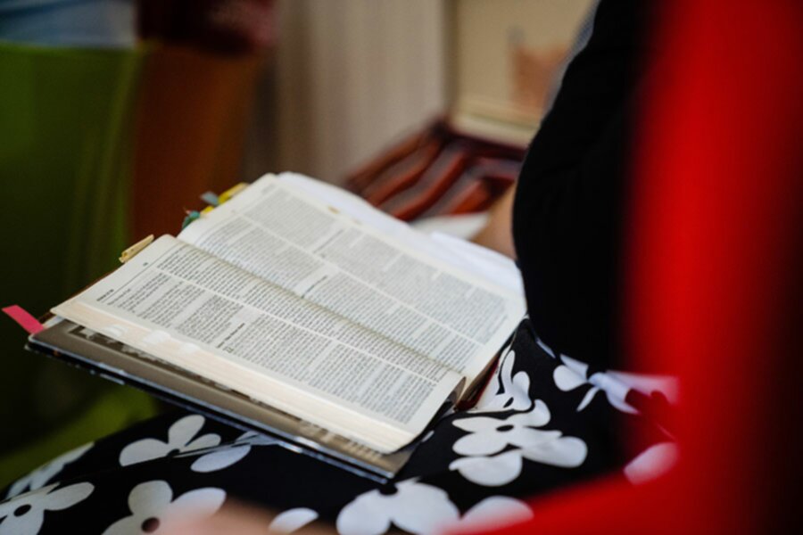 A photo of a Bible open on someone's lap with colourful tabs and bookmarks marking certain pages. The person is studying Biblical Hebrew and while their face cannot be seen, they wear a black top and a black and white floral skirt.