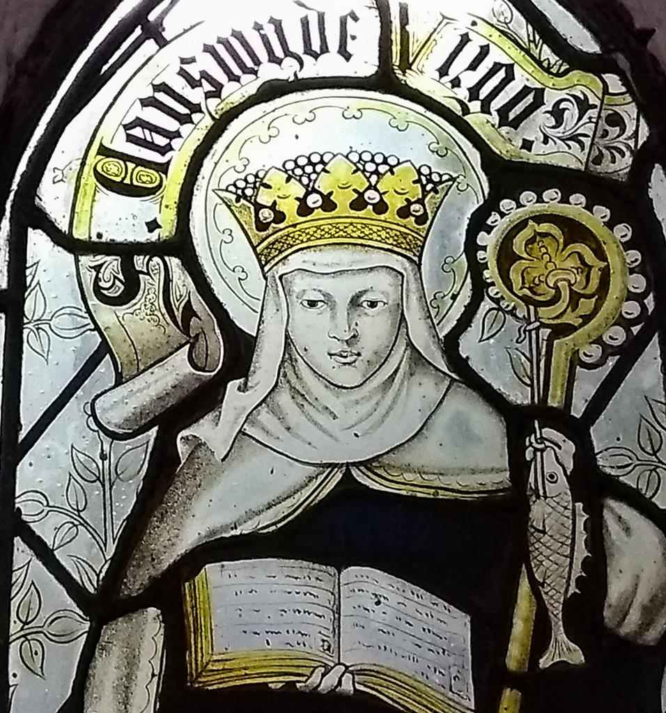 Stained glass in the Eanswythe Chapel at St Mary and St Eanswythe Church, by C E Kempe A stained glass window depicting St Eanswythe, an Anglo-Saxon woman wearing a head shawl, a golden crown and white cloack. She holds a curved staff and a fish in one hand and a book in the other.