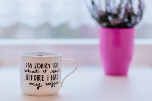 A coffee cup on a table with a pink vase.