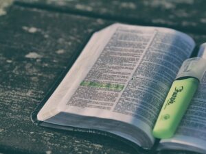 An opened Bible on a desk with a highlighter pen. Some of the text is highlighted in green.