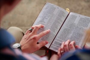An open Bible, held open by hands. Someone is reading it.