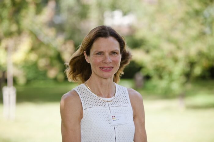 Becky Young, Head of Operations at St Augustine's College of Theology. She is standing outside surrounded by grass and trees, wearing a white sleeveless top.